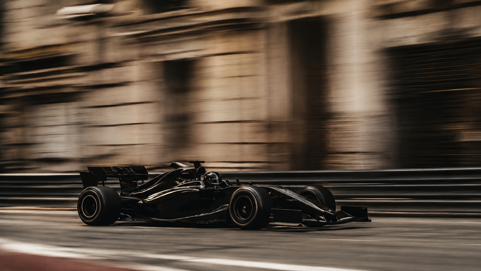 A single black open-wheel car passing at speed, the street circuit streaked behind it.